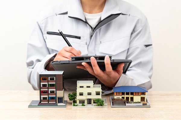 作業服を着た専門家が住宅模型を前にメモを取る様子。プロによる害虫駆除の事前調査とプランニングのイメージ。